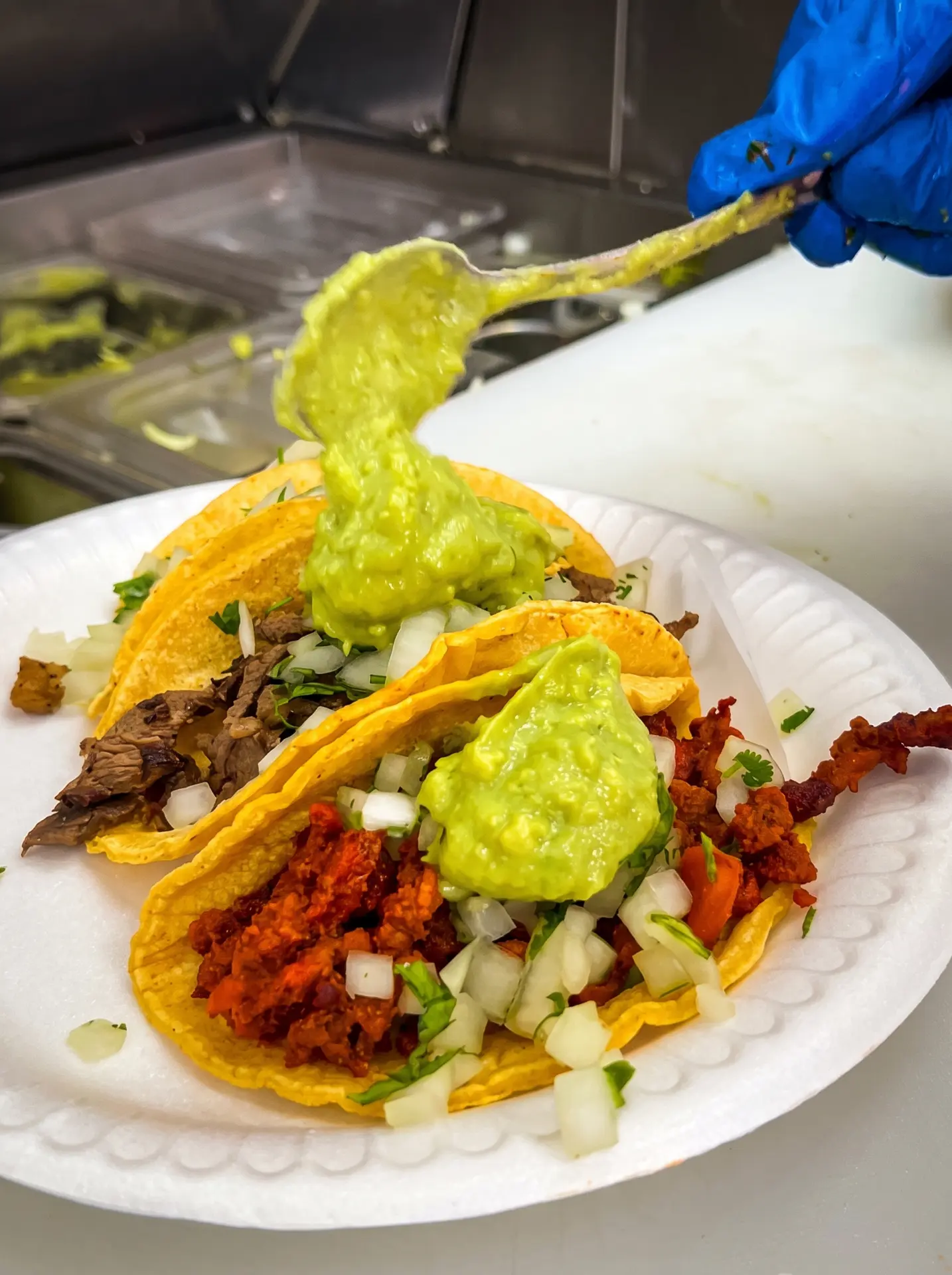 Asada and al pastor tacos being topped with fresh guacamole
