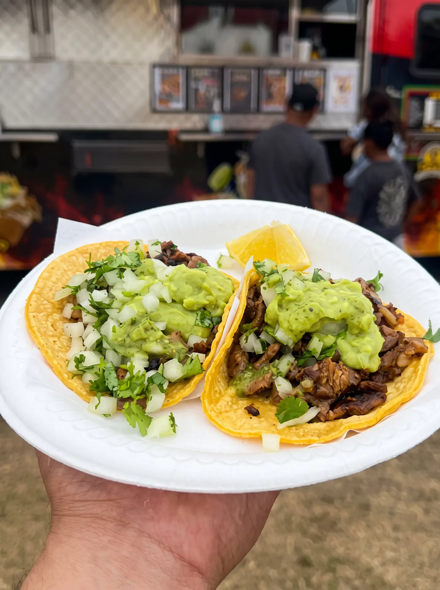 Two asada tacos topped with guacamole, onion and cilantro
